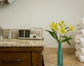 Corner of the sink and tub with Amenities on a silver tray. Yellow flowers in a blue vase sitting on the tile around the tub